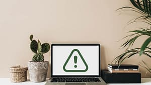 Laptop with a dark green caution symbol surrounded by books and plants