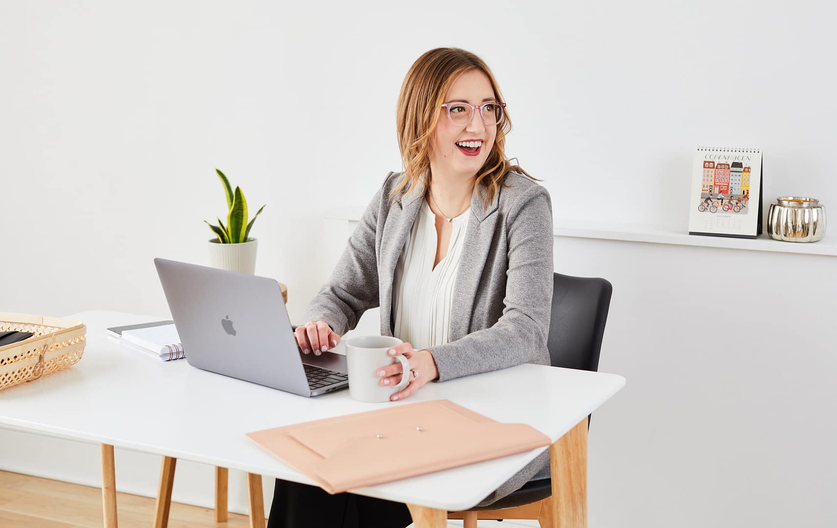 Charissa sits at a desk with a laptop, smiling and looks the the side